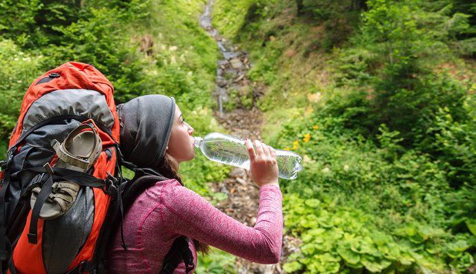 A day hiker stops on a hiking trail to take a drink from her water bottle. 
