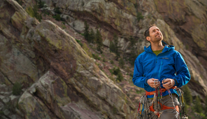Man in blue jacket stands holding carabiners