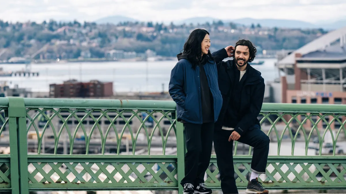 A man and woman, standing on a city bridge laughing