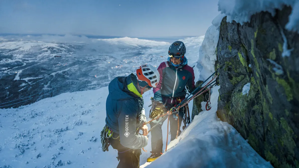 Two people standing on a mountainside at dusk, engaging with each other
