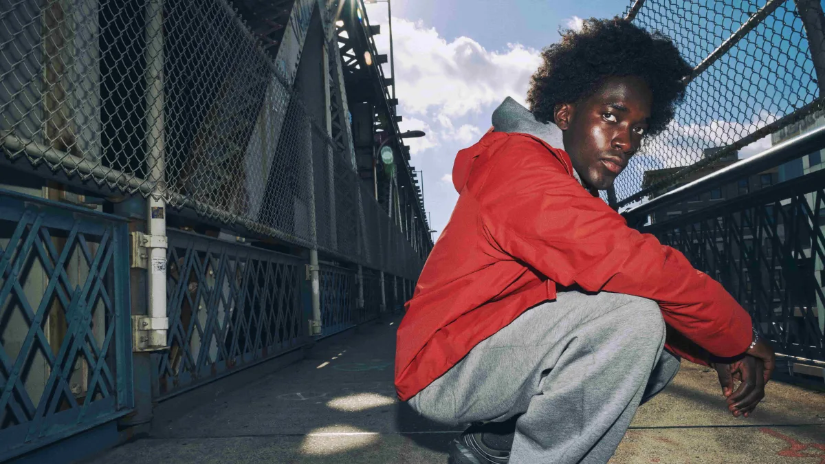 Man sitting in front of a city chain-link fence, wearing a red GORE-TEX Jacket