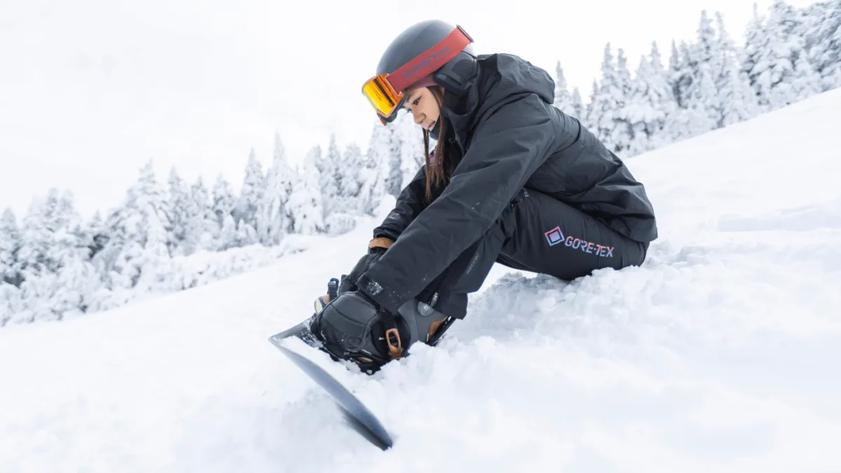 Woman adjusting her snowboarding boots in the snow